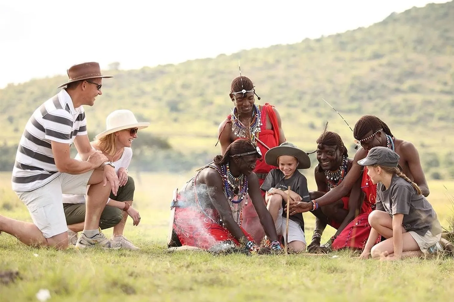A family with two children sitting on the grass with Maasai women during a village visit on safari in Tanzania