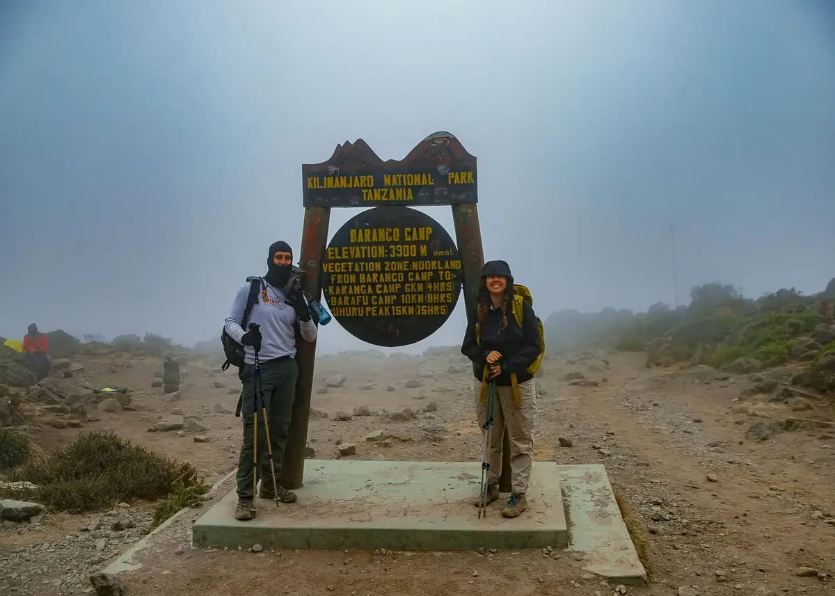 Two climbers at the Barranco Camp sign, 3,900 m, in mist on Kilimanjaro
