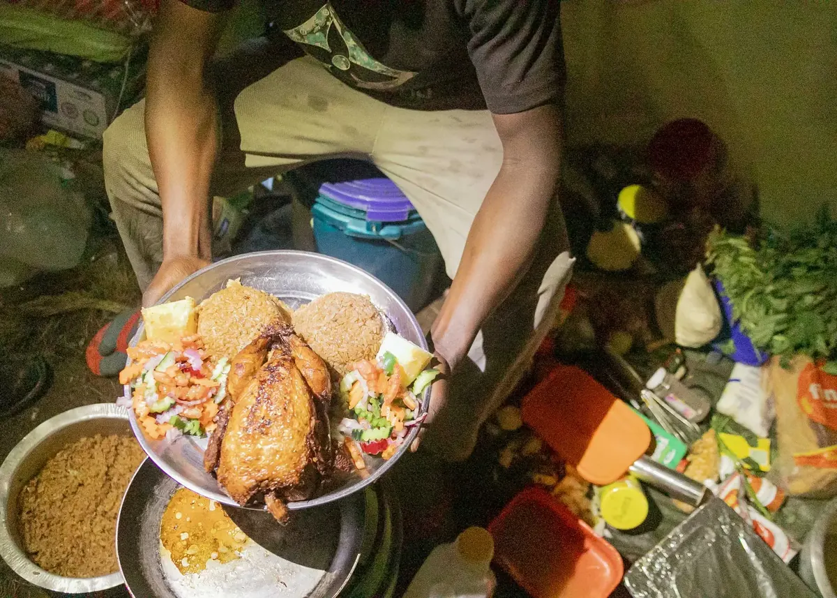 A Kilimanjaro cook holding a plate of roast chicken, spiced rice and fresh salad for dinner