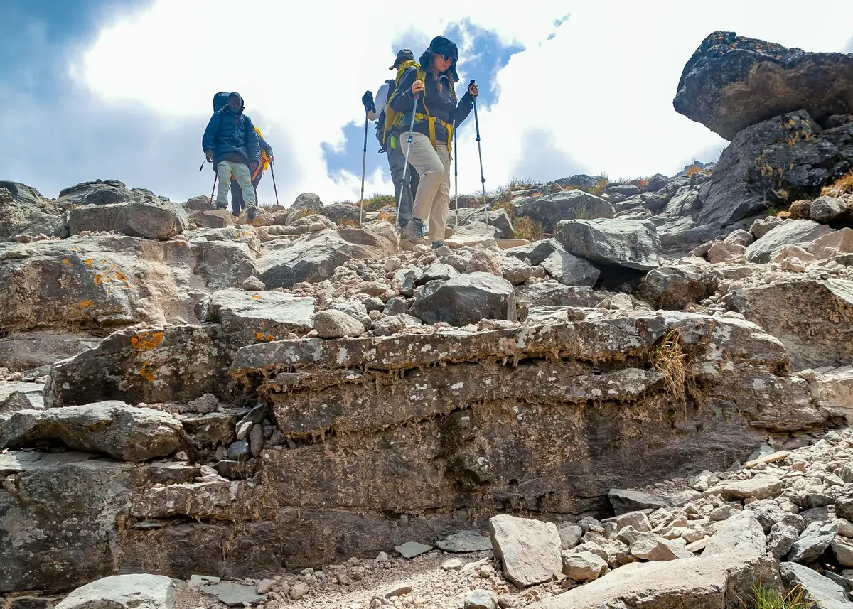 A guide and two climbers with trekking poles picking their way down a rocky section of trail on Kilimanjaro