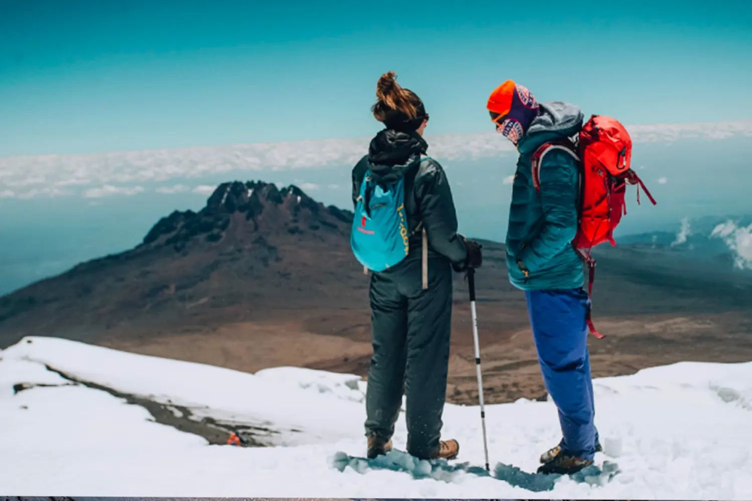 Two climbers standing in the snow near the summit of Kilimanjaro, with Mawenzi peak and the clouds behind them