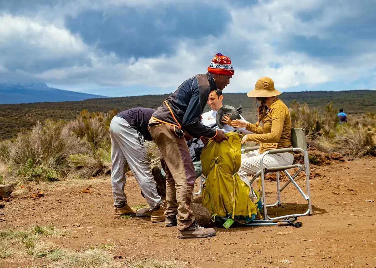 A Jaynevy Tours guide and porter helping a couple with their backpacks at a lunch stop on Kilimanjaro's moorland