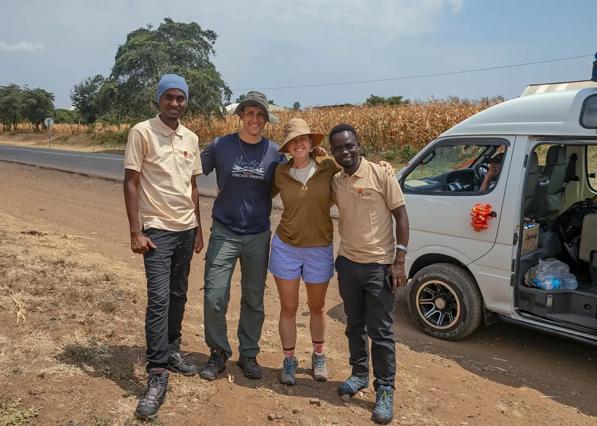 A honeymoon couple with two Jaynevy Tours guides beside the climb vehicle decorated with a ribbon, on the way to the mountain