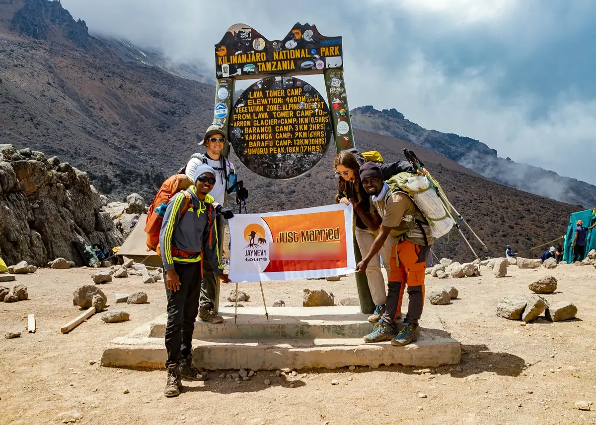 A just-married couple and their crew holding a Just Married banner at the Lava Tower Camp sign, 4,600 m, on Kilimanjaro
