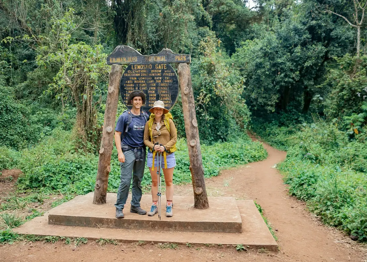 Two climbers at the Lemosho Gate sign of Kilimanjaro National Park, at 2,100 m in the montane forest
