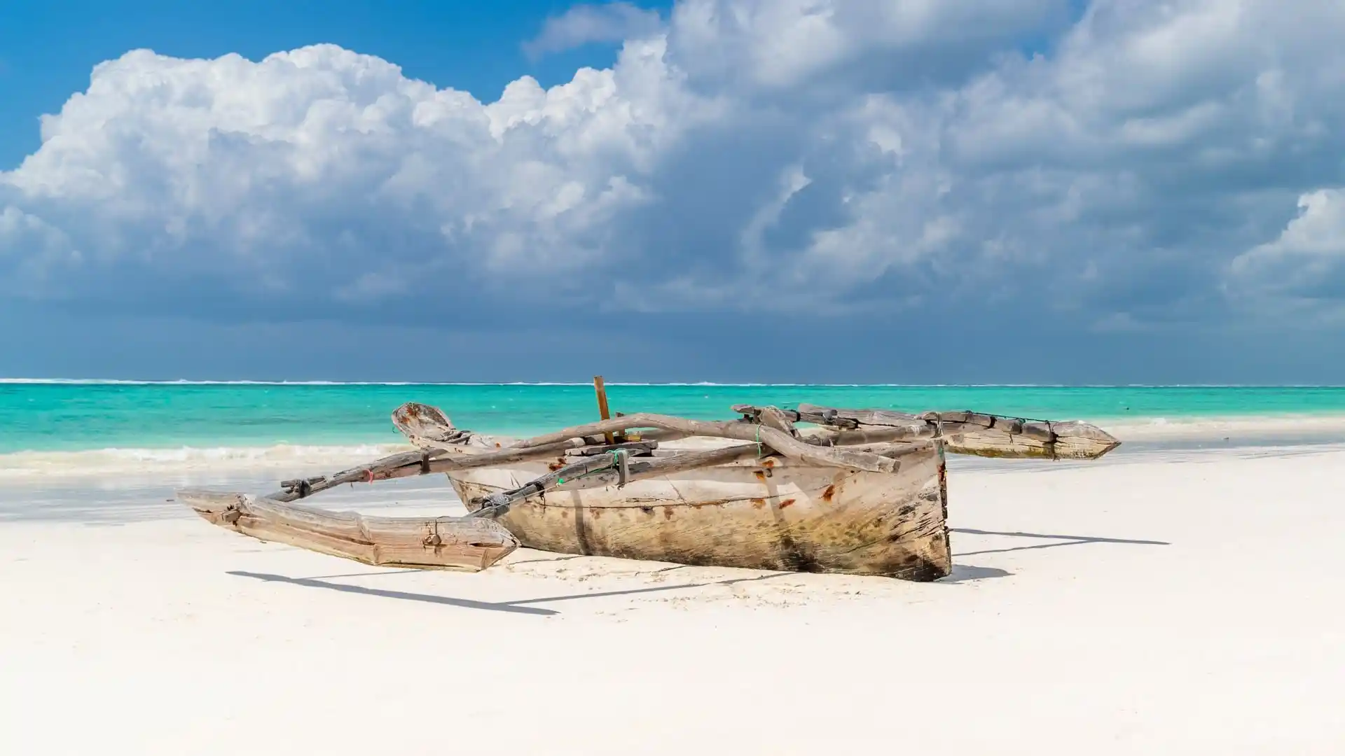 A wooden outrigger dhow on a white-sand beach with turquoise water on Zanzibar's east coast